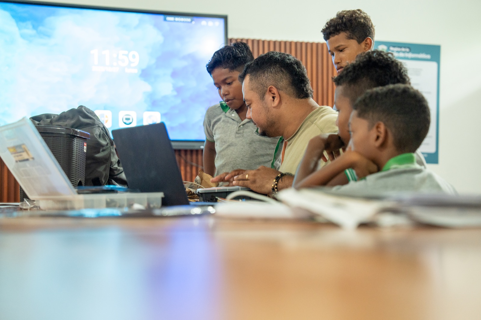 Estudiantes trabajan con su docente alrededor de un computador y materiales tecnológicos.